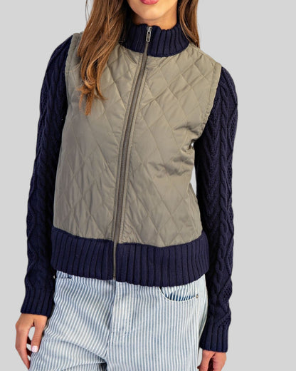 Navy and olive mixed-media jacket with quilted body, navy cable knit sleeves, and ribbed trim with a zipper front.