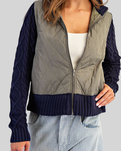 Navy and olive mixed-media jacket with quilted body, navy cable knit sleeves, and ribbed trim with a zipper front worn with a white tee shirt.