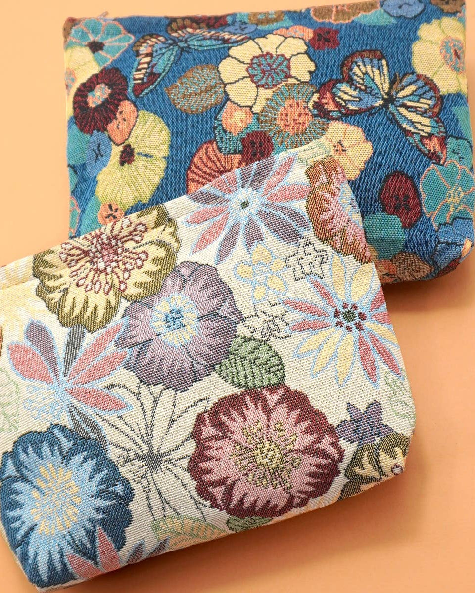 A beige and a blue floral embroidered make-up / toiletry bags on peach background.