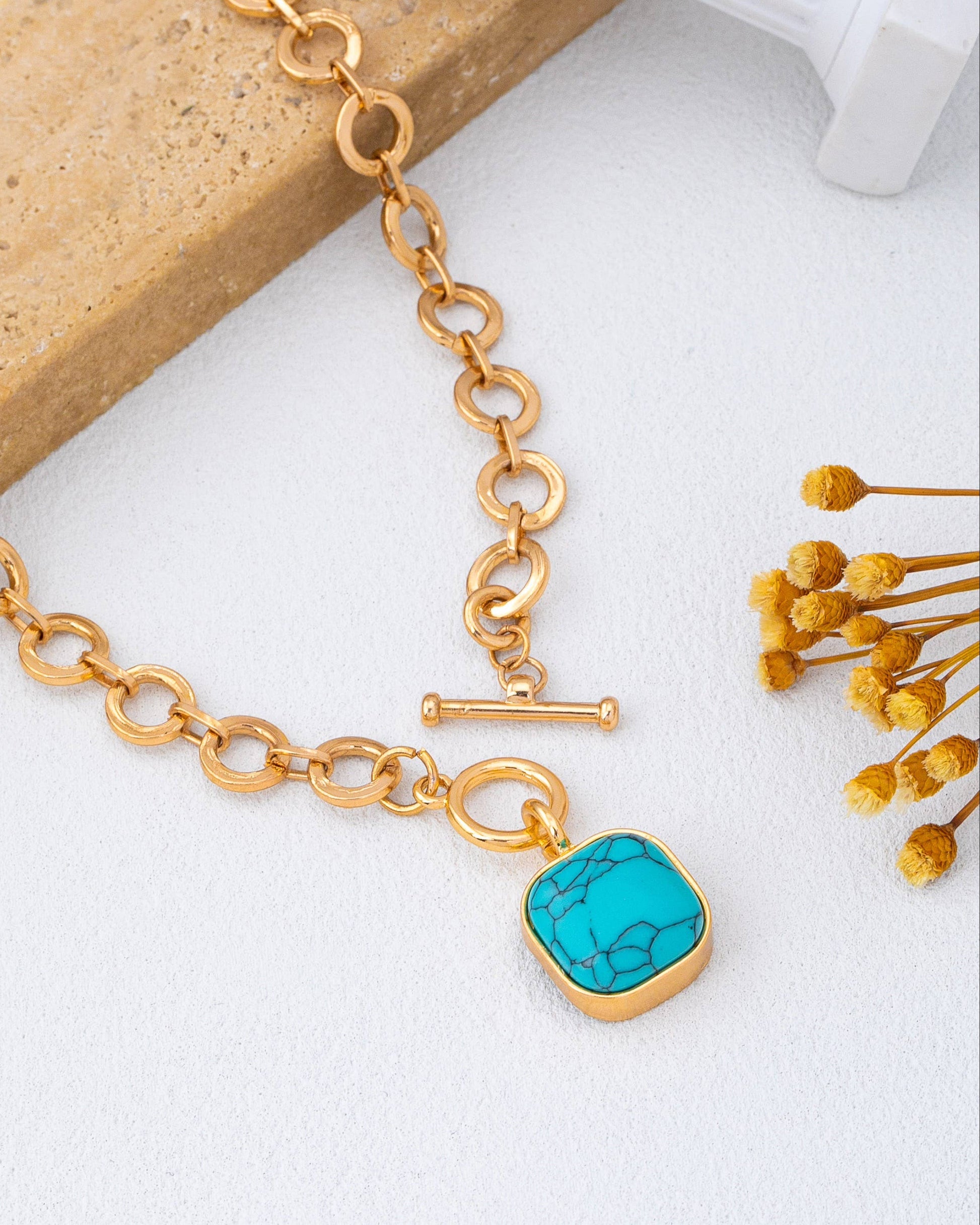 Gold toggle necklace with a turquoise pendant on a light background.