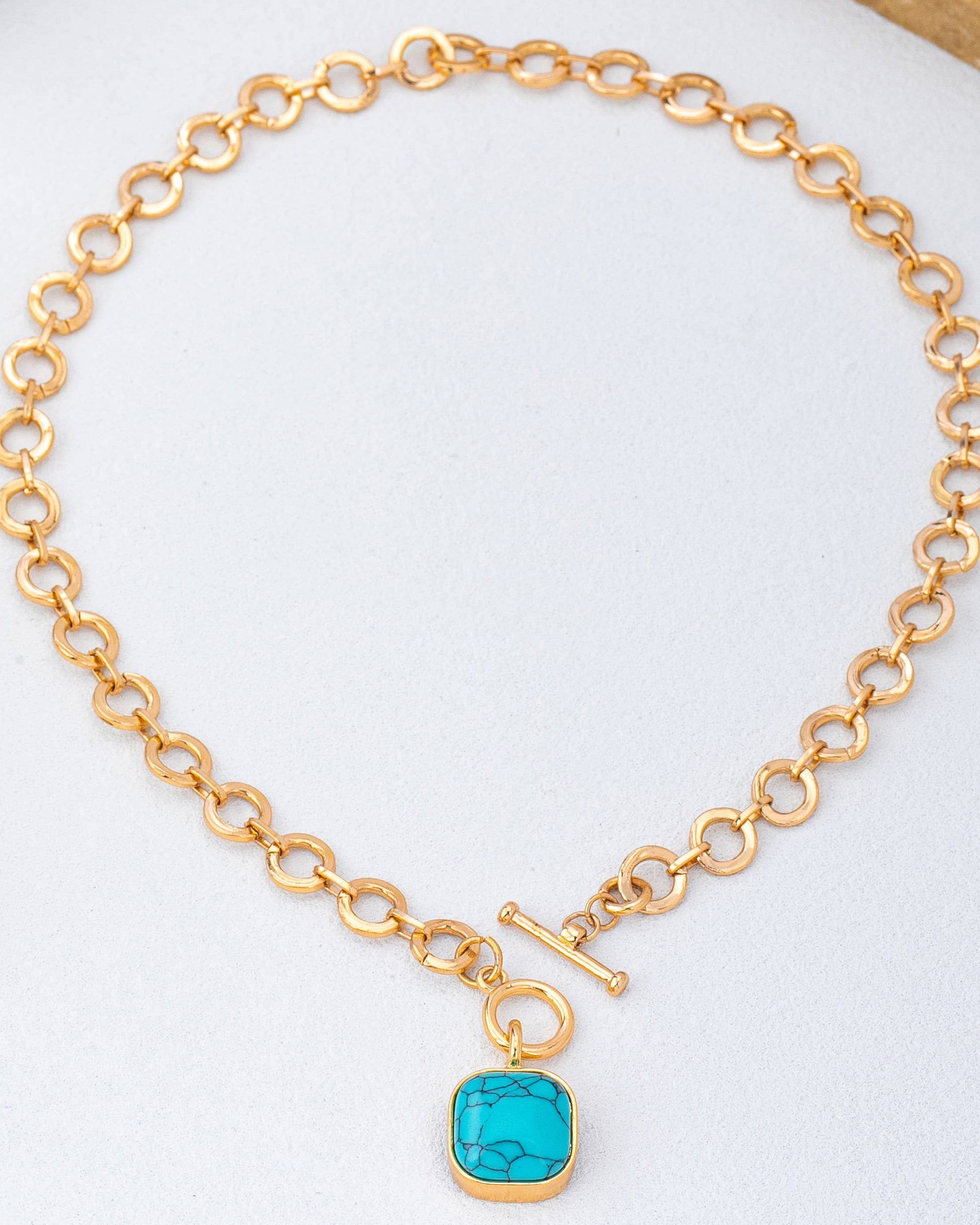 Gold chain toggle necklace with a turquoise pendant on a white background.