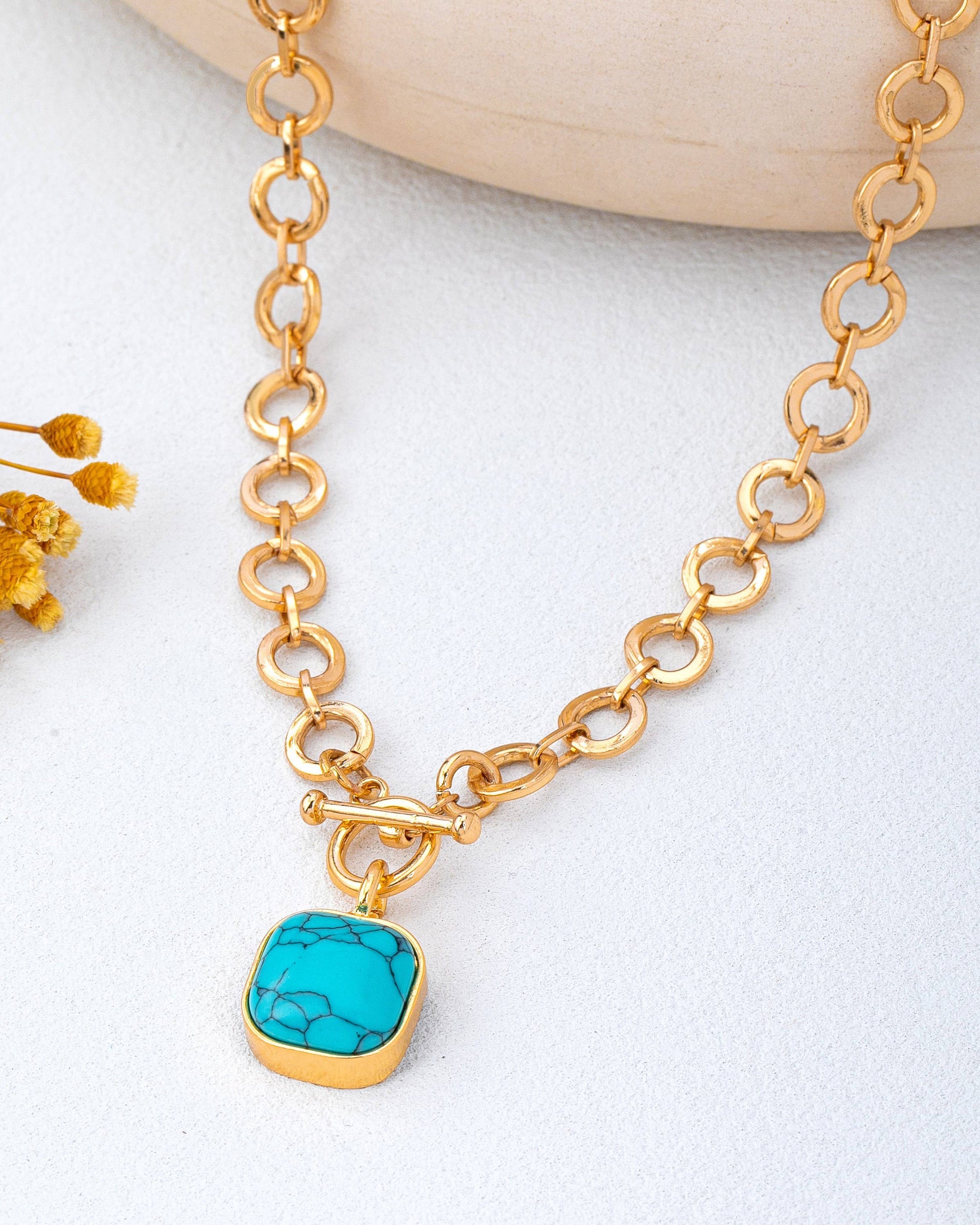 Gold toggle necklace with a turquoise pendant on a light background.