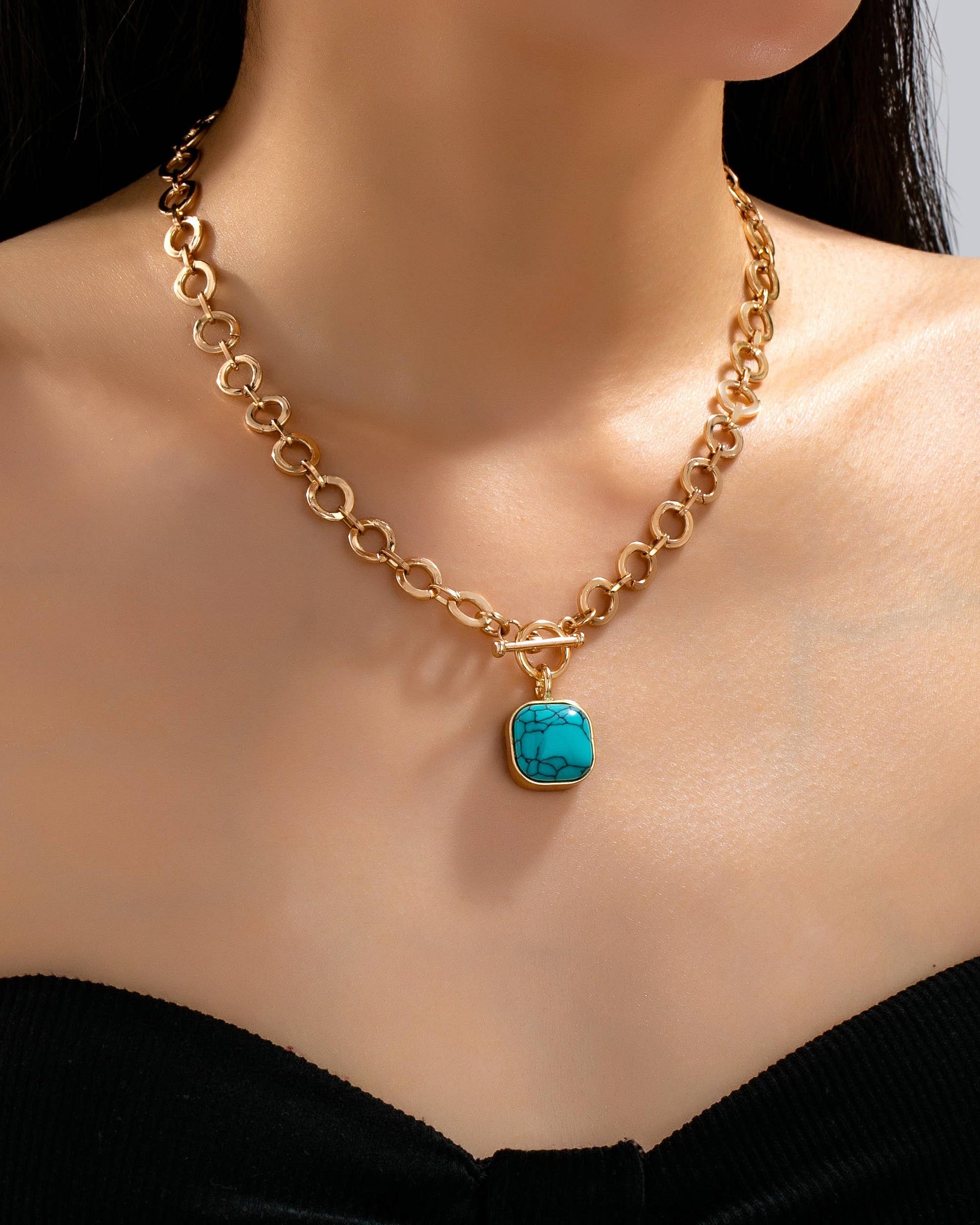 Gold toggle chain necklace with a turquoise pendant on a model wearing a black top.