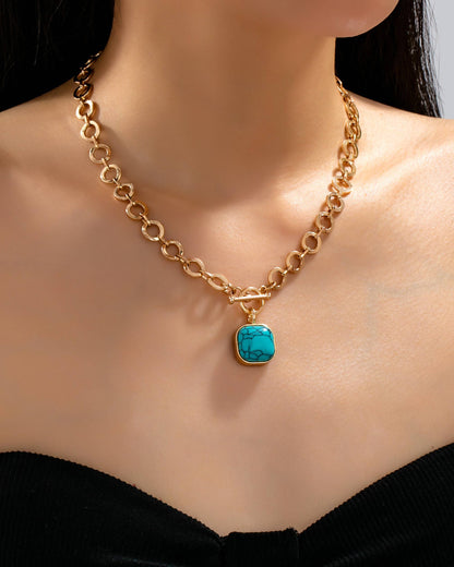 Gold toggle chain necklace with a turquoise pendant on a model wearing a black top.