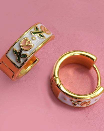 Gold hoop earrings with floral design on a pink background.
