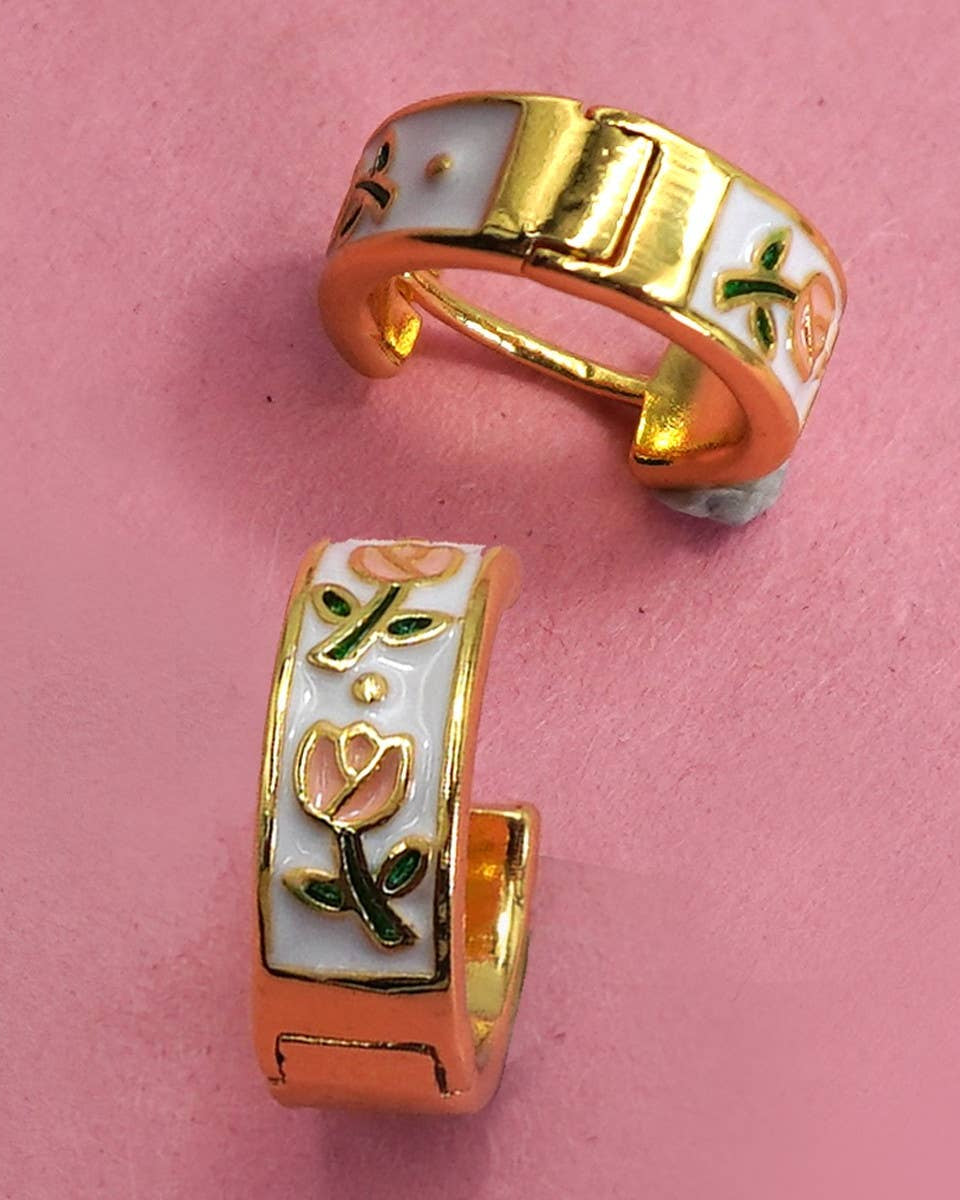 Gold and white huggie hoop earrings with floral designs on a pink background.
