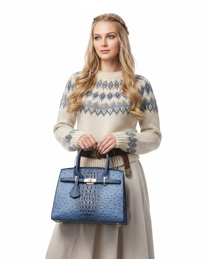 A blonde model holding an ostrich and croc embossed vegan leather satchel handbag in a navy blue tone with gold hardware.