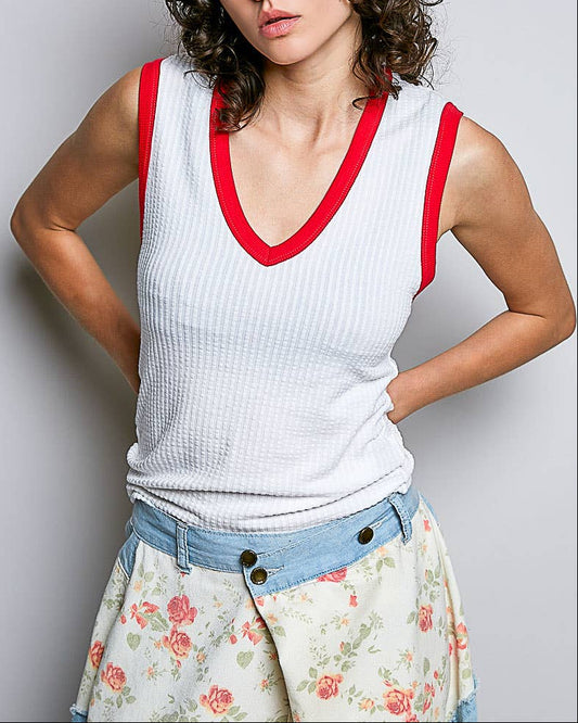 Woman wearing a white tank top with red trim and a floral skirt on a plain background
