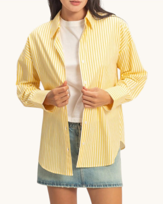 Woman wearing a yellow striped shirt over a white top and denim skirt on a white background